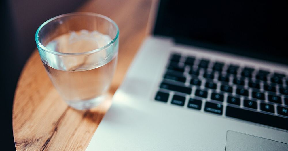 A clear glass of water sits next to a laptop