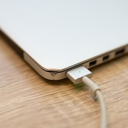 Charging a laptop with a USB cable on a wooden table in a cozy environment during daytime