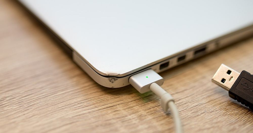 Charging a laptop with a USB cable on a wooden table in a cozy environment during daytime