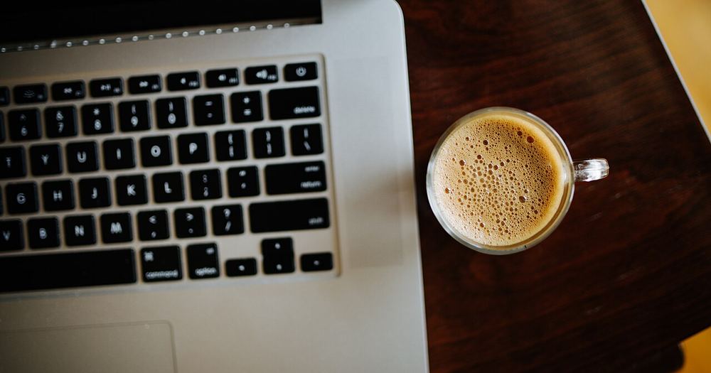 Coffee cup next to laptop on wooden table in cozy indoor workspace during daytime