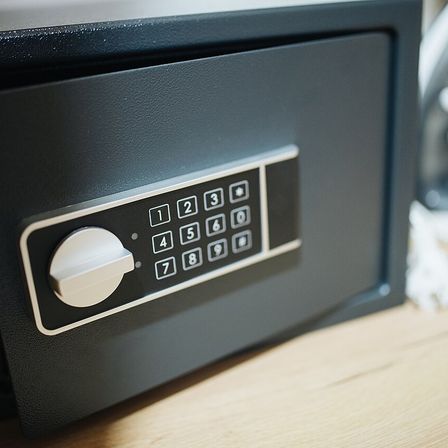 A black security safe with a numeric keypad is set within a wooden cabinet